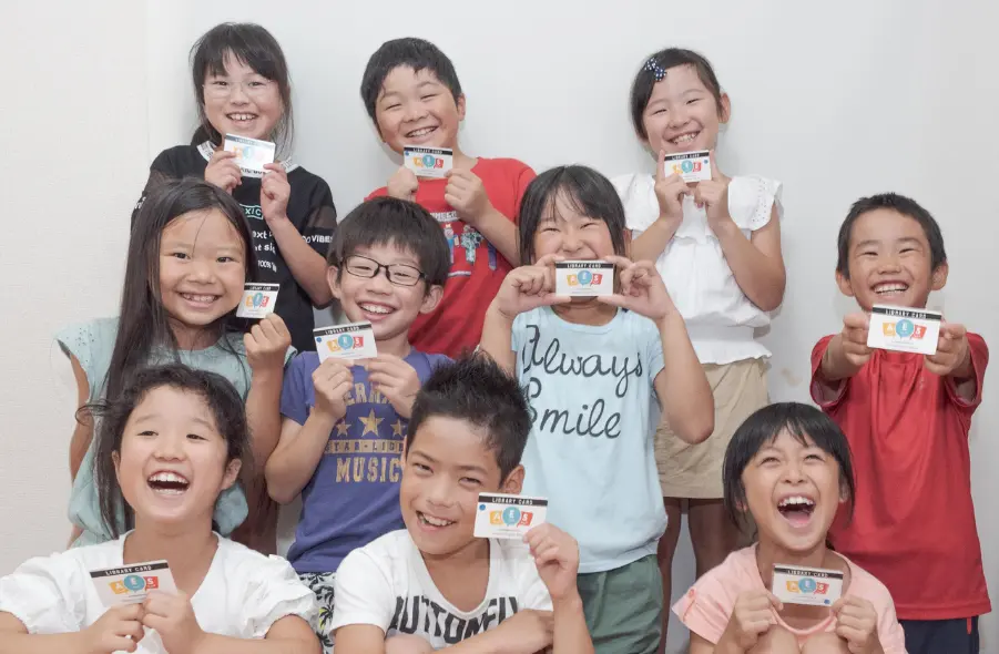AES英会話で英語学習の達成カードを手に笑顔を見せる小学生たち。垂井町の子ども英語教室で楽しく学んでいます。
